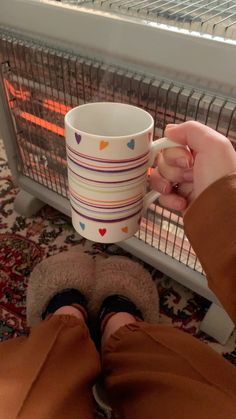 a person holding a coffee cup in front of a heater