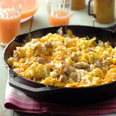 a skillet filled with eggs and sausage on top of a table next to orange juice