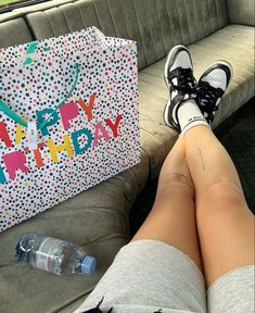 a person sitting on a couch with their legs crossed, next to a birthday bag