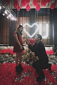 a man kneeling down next to a woman in a room with balloons and streamers