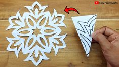 someone cutting out paper snowflakes on a wooden table