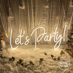 the words let's party are lit up in front of a backdrop with flowers