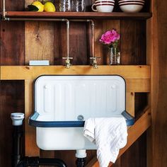 a white sink sitting under a wooden shelf next to a wall mounted faucet