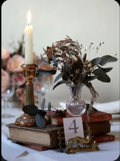 a table topped with books and a vase filled with flowers next to a lit candle