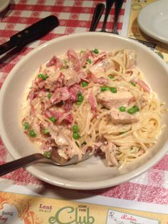 a white bowl filled with pasta and meat covered in sauce on top of a checkered table cloth