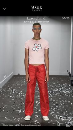 a man standing in front of a white wall wearing red pants and a pink t - shirt