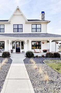 a white house with lots of windows and plants on the front lawn, along with graveled walkway