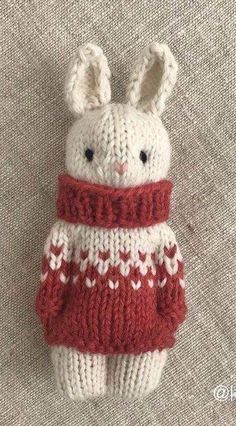 a knitted bunny wearing a red and white sweater on top of a gray surface