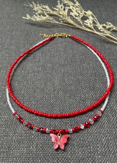 two necklaces with red beads and a pink butterfly on one bead, the other is