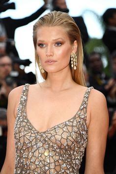 a woman with blonde hair and earrings standing in front of photographers