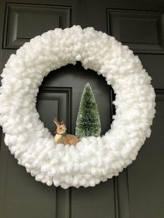 a white yarn wreath with a small christmas tree in the center and a fake deer on top