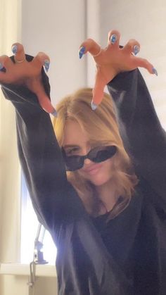 a woman with her hands in the air while wearing sunglasses and holding up two fingers