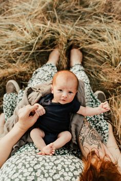 a woman holding a baby in her arms while laying on top of a field of dry grass