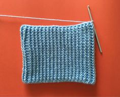 a crochet square with a knitting needle next to it on an orange surface