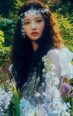 a woman with long hair wearing a white dress and flowers in her hair is sitting on the ground