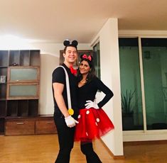 a man and woman dressed up as mickey and minnie mouse in a living room with wood floors