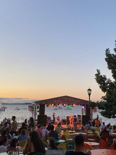 a group of people sitting at tables in front of the ocean with an outdoor concert set up