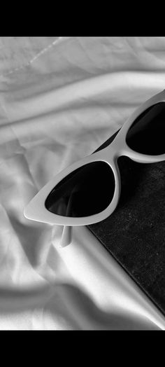 a pair of white sunglasses sitting on top of a black and white cloth covered bed