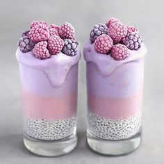 two desserts with raspberries on top are in glass jars, one is pink and the other is blue