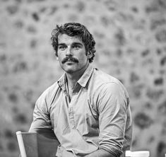 black and white photograph of a man with a mustache sitting on a chair in front of a wall