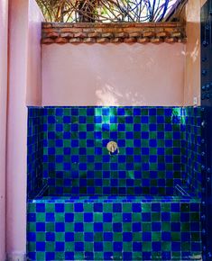 a blue and green tiled bathtub in a pink walled shower stall with plants growing on the wall