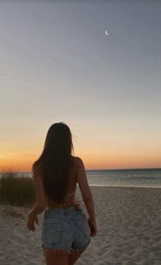 a woman walking on top of a sandy beach next to the ocean at sunset or dawn