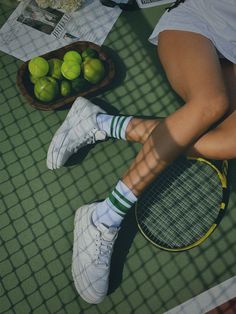 a woman sitting on the ground with tennis rackets and limes in front of her