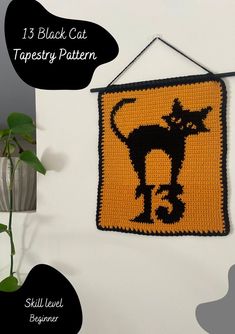 a crocheted black cat tapestry hanging on a wall next to a potted plant