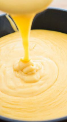 a yellow sauce being poured into a black pot filled with cheesecake batter and melted cheese