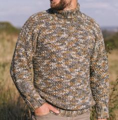 a man standing in a field wearing a sweater