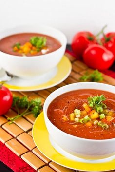 two bowls of soup on a table with tomatoes and other vegetables in the back ground