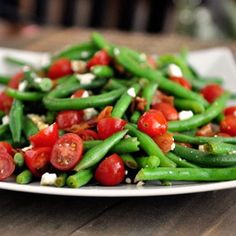 a white plate topped with green beans and cherry tomatoes on top of a wooden table