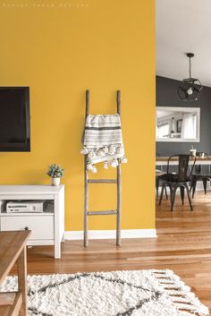 a living room with yellow walls and white rugs on the hardwood floor next to a ladder