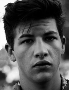 a black and white photo of a young man with short hair looking at the camera