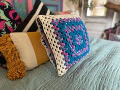 three pillows on top of a bed with blue and white sheets, one is crocheted