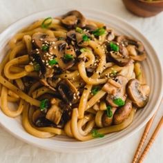 a white plate topped with noodles covered in mushrooms and green onions next to chopsticks