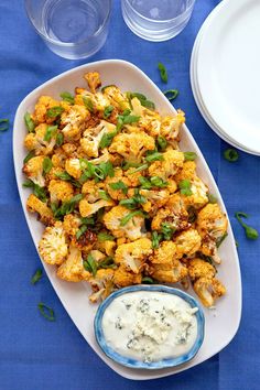 a white plate topped with cooked cauliflower next to a bowl of ranch dressing