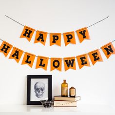 an orange happy halloween banner hanging on a wall next to a book shelf and framed photograph