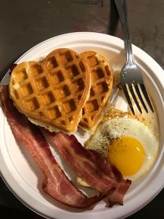 a white plate topped with waffles, bacon and an egg next to a fork