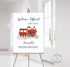 a red train birthday sign on an easel in front of a white wall with the words welcome aboard