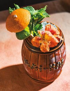 an orange flower in a wooden vase with leaves and flowers on the top, sitting on a table