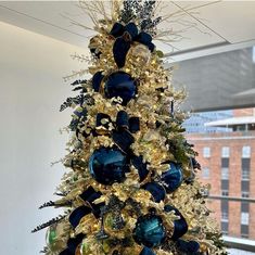 a blue and gold christmas tree in an office building with windows overlooking the city below