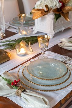 the table is set for christmas dinner with white and gold plates, napkins, silverware and candlesticks