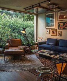 a living room filled with furniture next to a window covered in lots of plants and trees