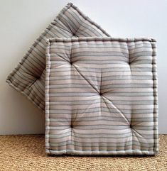 a square shaped cushion sitting on top of a carpeted floor next to a wall