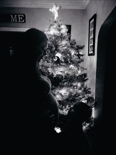 a pregnant woman standing in front of a christmas tree