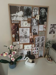 a bulletin board with pictures and flowers in a vase on a table next to a coffee cup