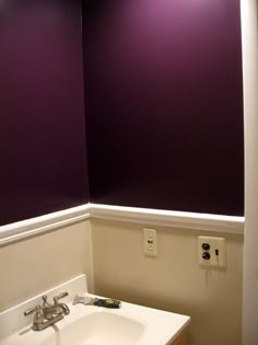 a white sink sitting under a purple wall in a bathroom next to a light switch