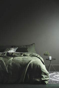 a bed with green sheets and pillows in a dark room next to a small table