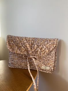 a brown and white flowered purse sitting on top of a wooden table next to a lamp